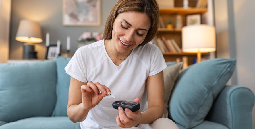 young woman smiling as she tests her blood sugar at home using a pin prick monitor